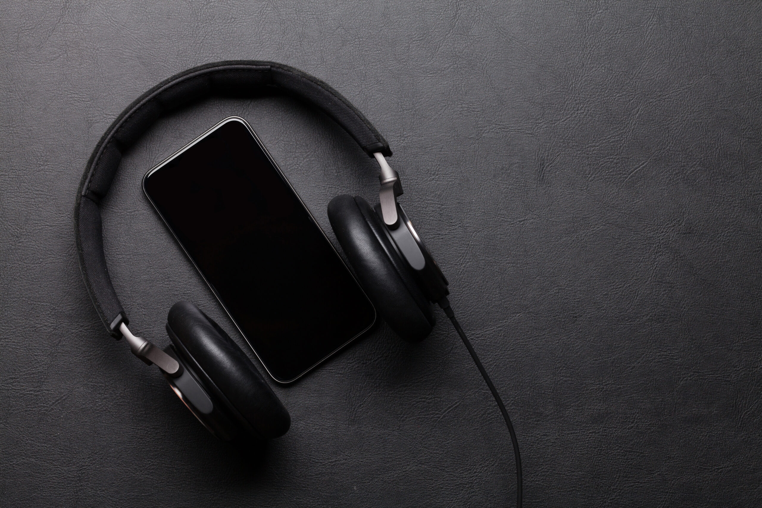 Headphones and smartphone on leather desk table. Top view with copy space